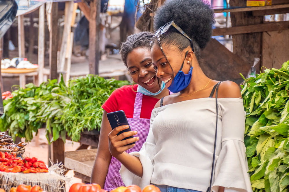 deux femmes visionnant du contenu sur un telephone dans un marche africain local 1 1