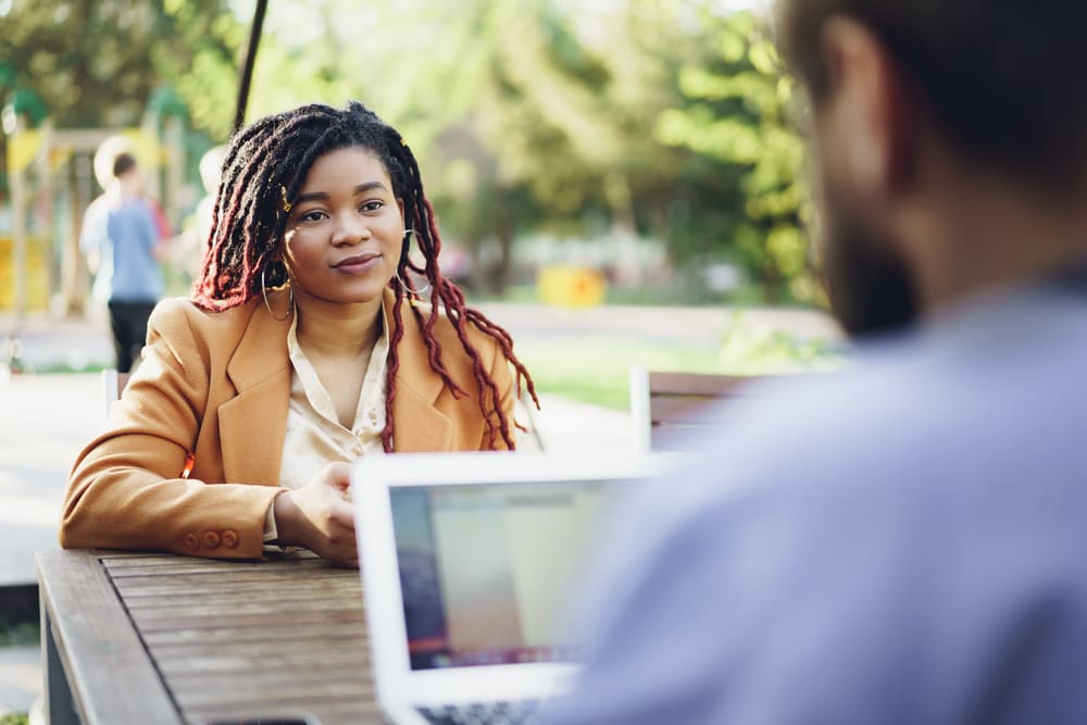 souriante jeune femme africaine assise a une table dans un cafe avec un homme de race blanche et discutant1