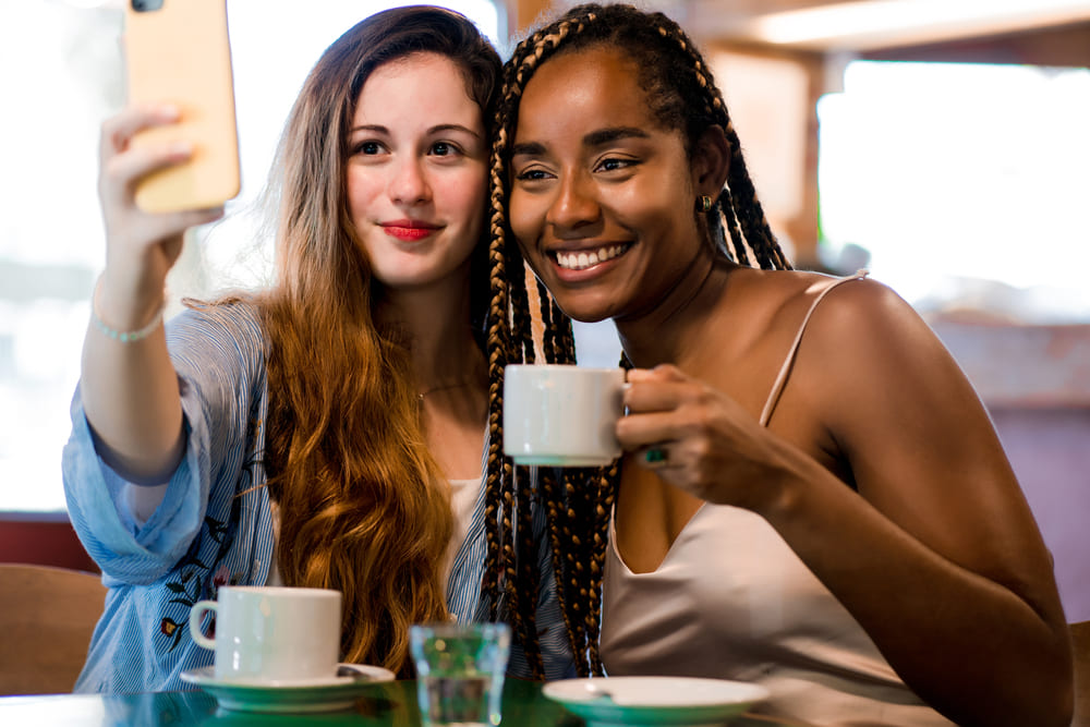 Meet singles in France 25 deux amis prenant un selfie avec un telephone portable tout en buvant une tasse de cafe dans un cafe notion d amis1